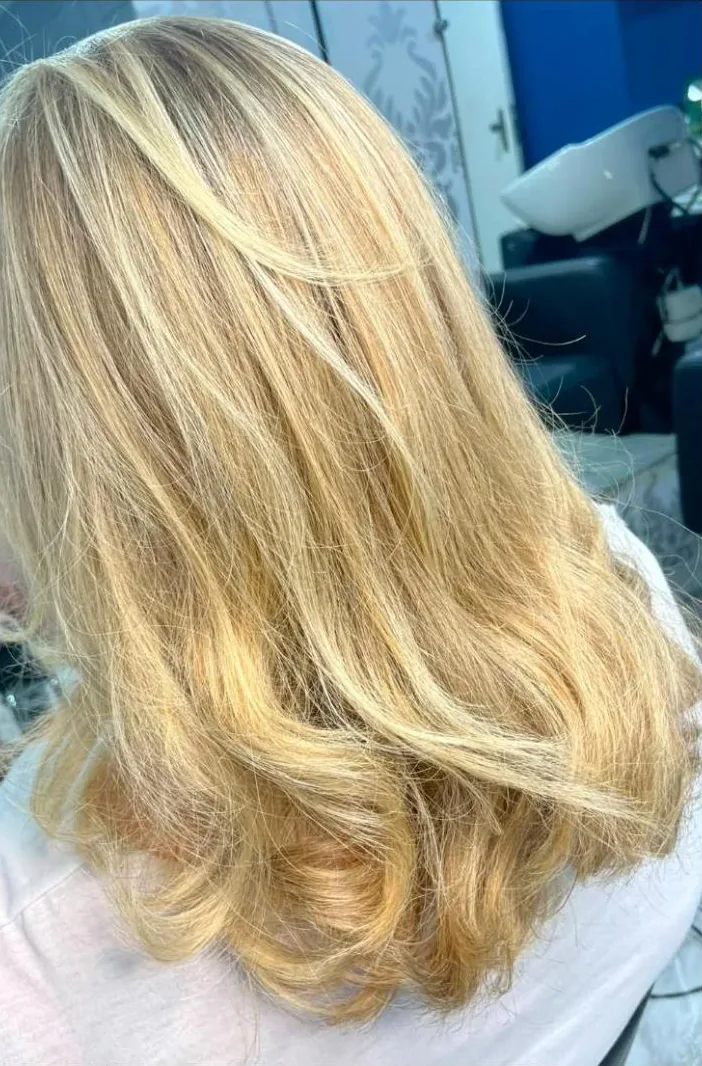 Cabelo loiro iluminado com pontas onduladas, visto de costas, no salão